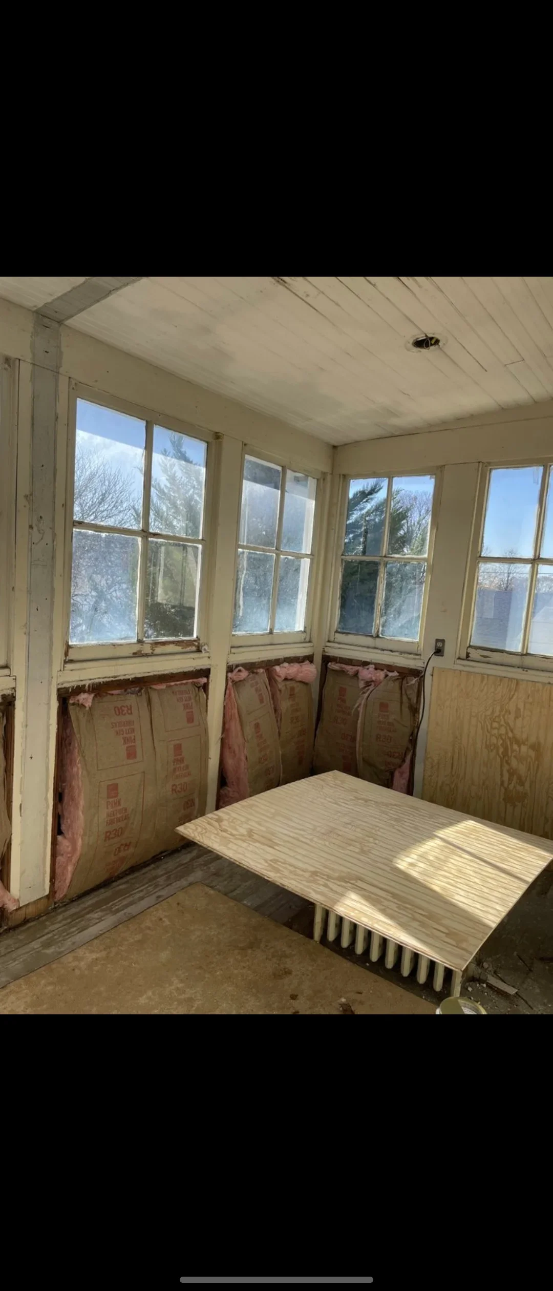 Sunroom interior with primed drywall, sealed windows, and red rosin paper protection during painting preparation
