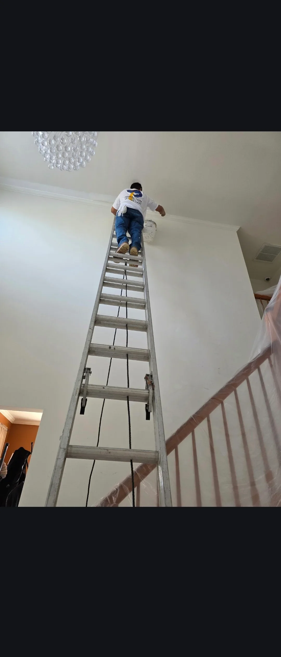 Painter on ladder applying fresh white paint to high interior ceiling and walls