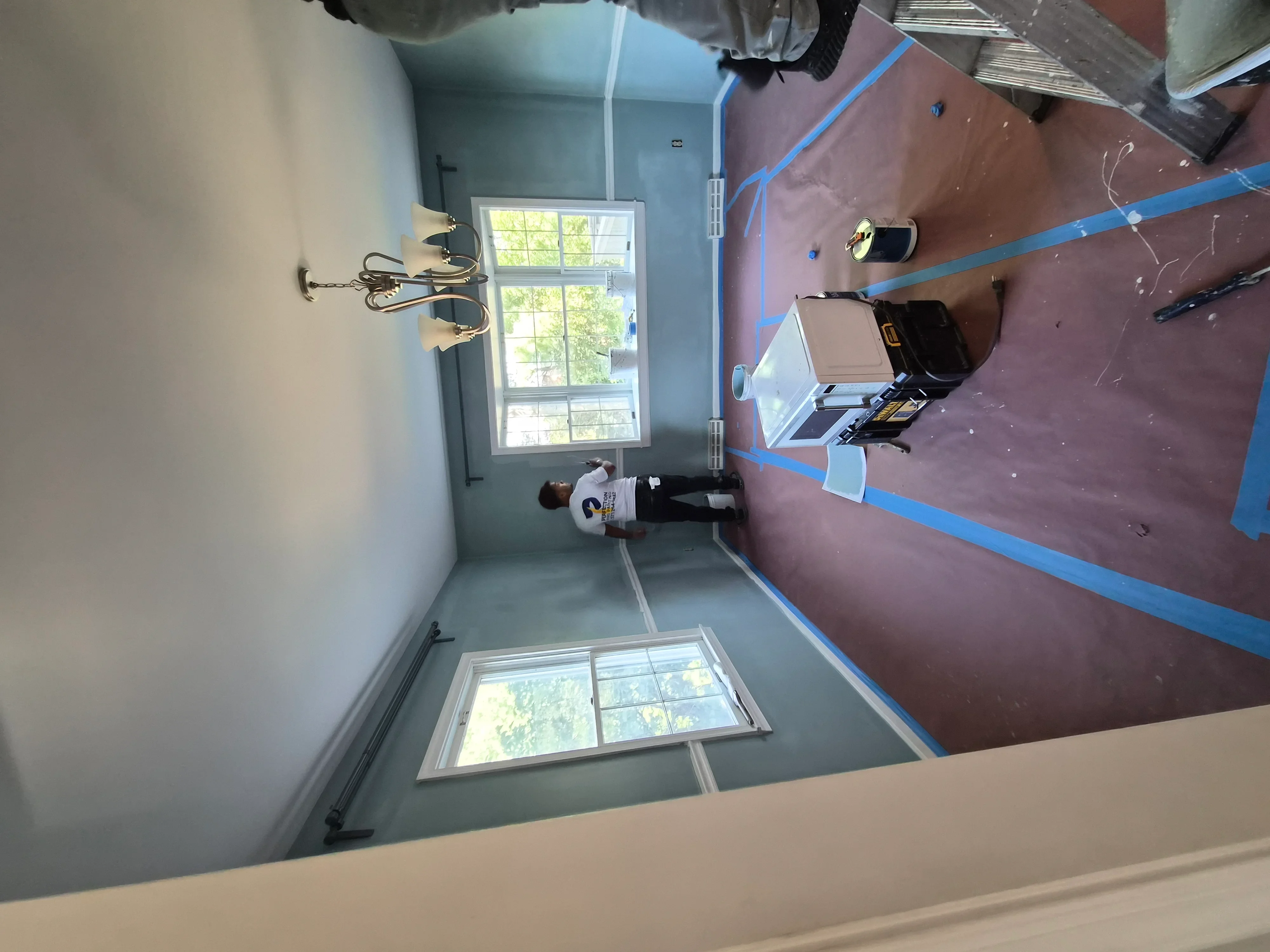 Interior room with primed drywall, blue painter's tape, and two windows during active painting project