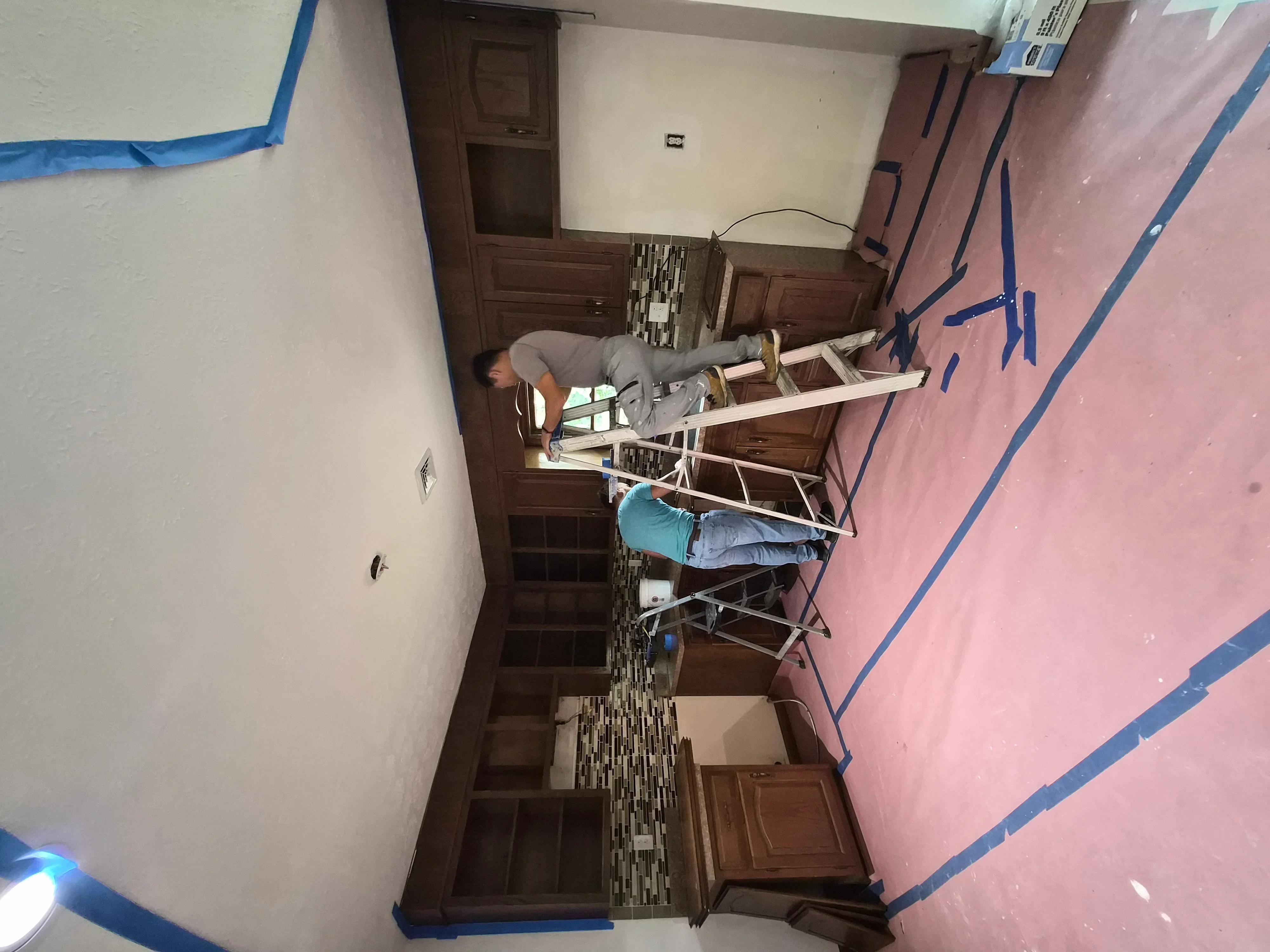 Interior room with cream and pink painted walls, dark wood trim, blue painter's tape, and work-in-progress drywall preparation