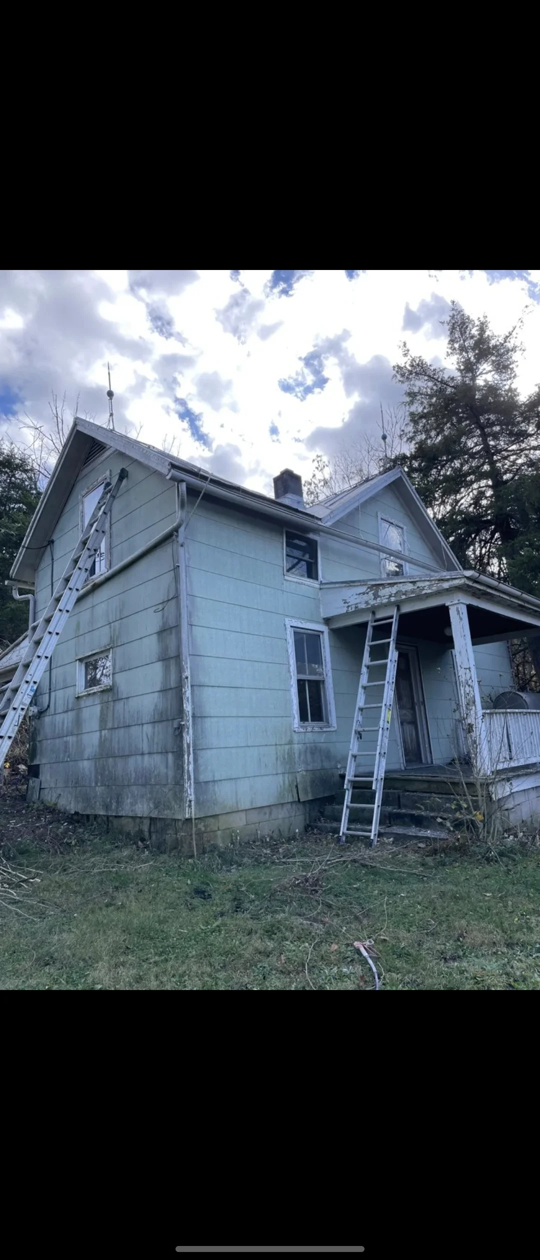 Two-story house with blue siding and ladders set up for exterior painting work