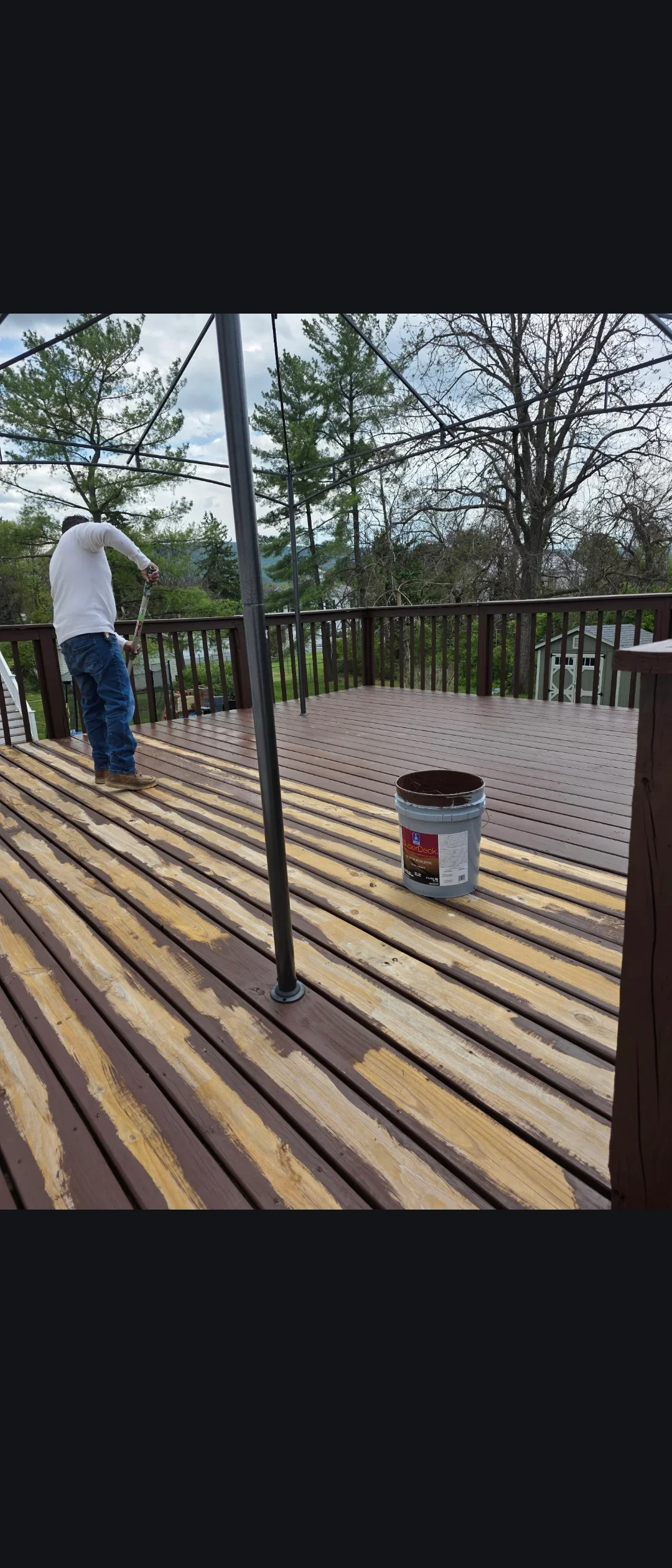 Deck staining in progress with two-tone brown stain on composite boards and dark railings