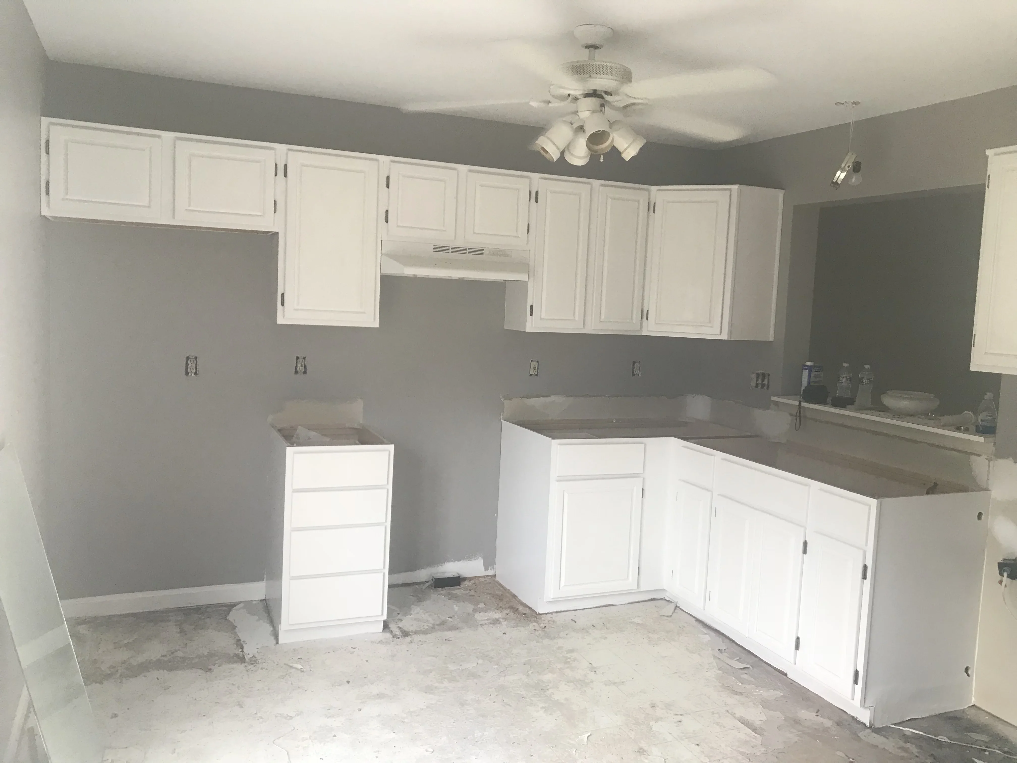 White painted kitchen cabinets with gray walls and ceiling fan in renovation