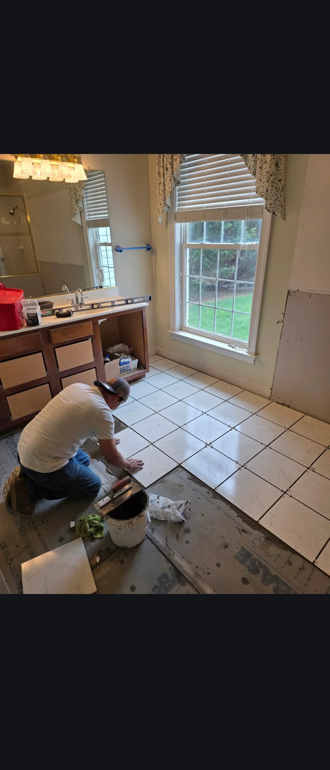 Worker installing ceramic floor tiles in bathroom with white subway tile pattern