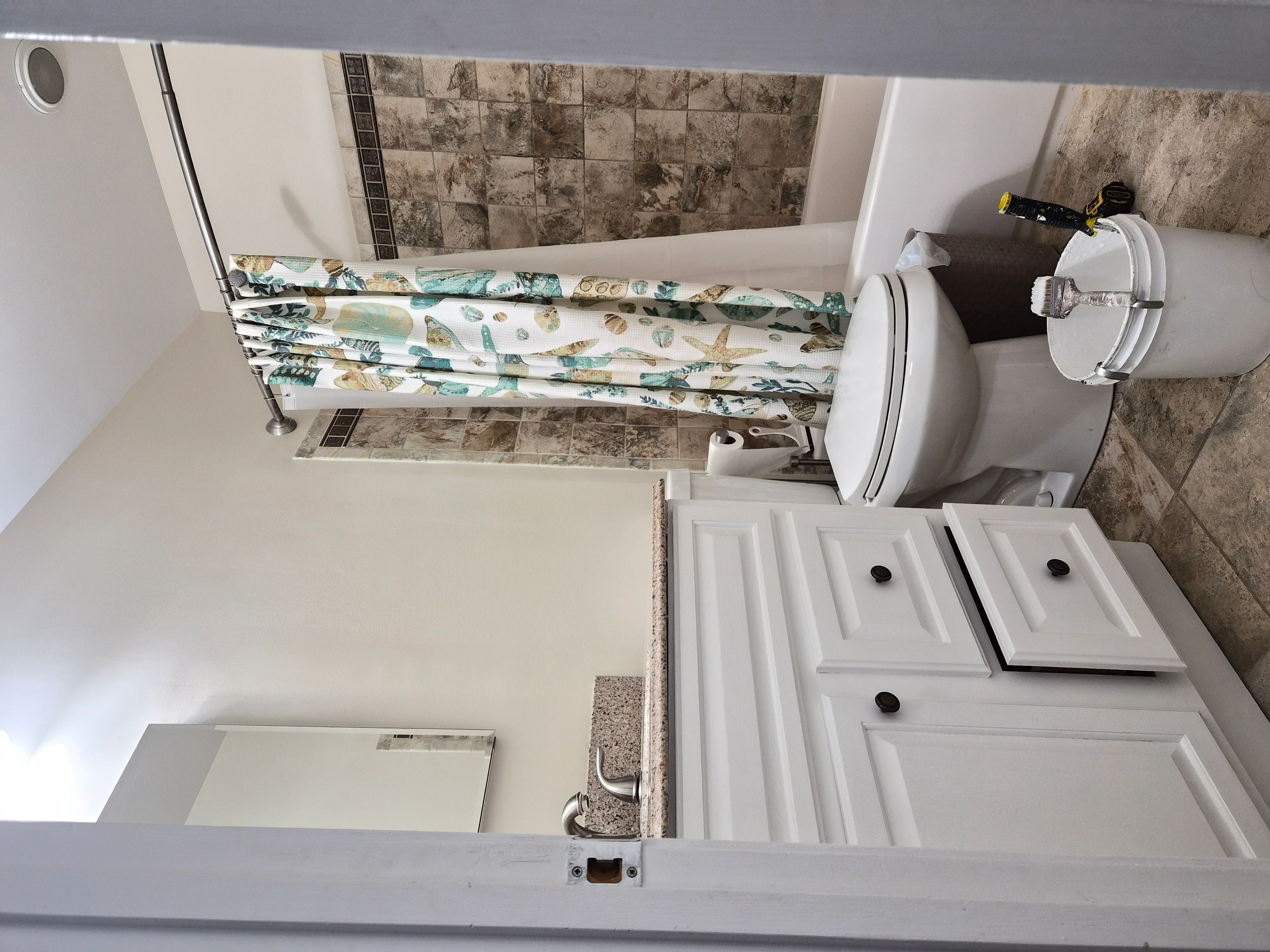 Bathroom with white painted walls, travertine tile backsplash, white vanity cabinets, and bathtub