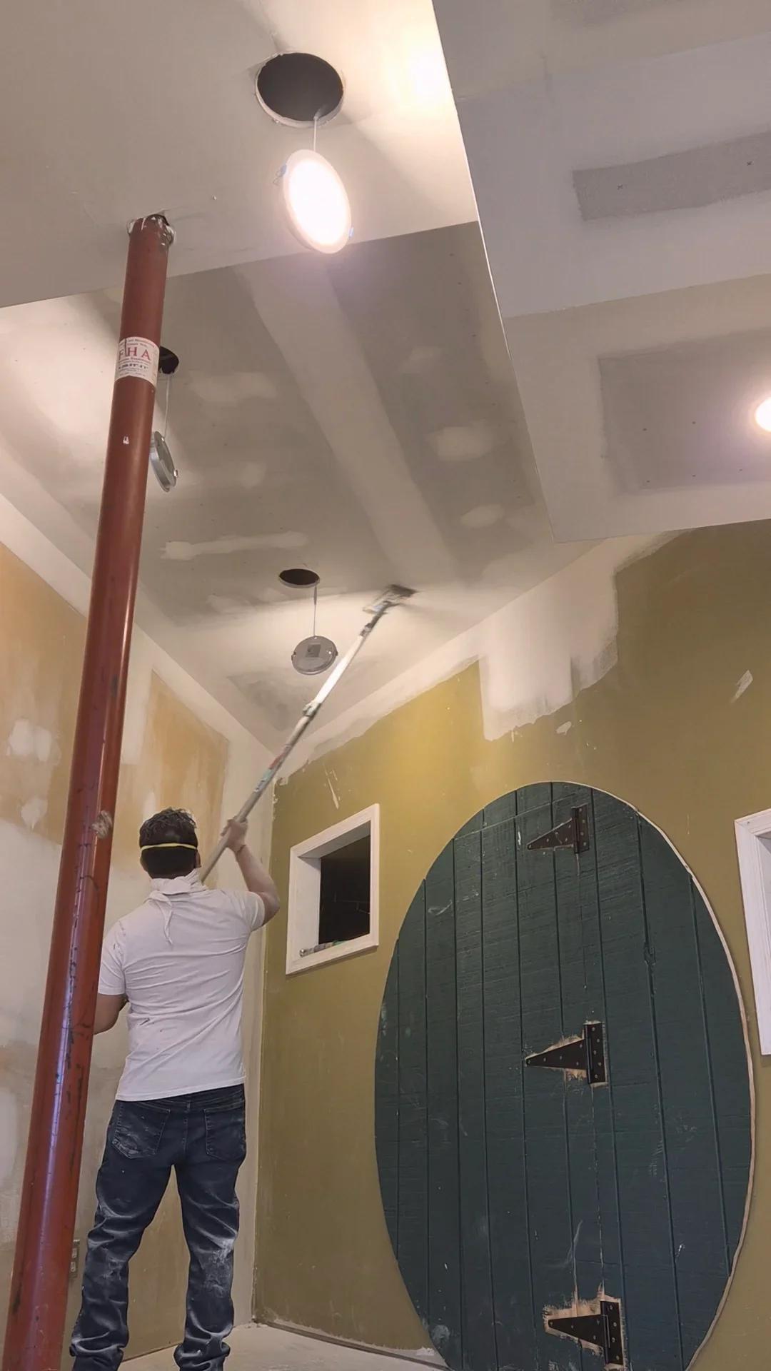 Worker painting interior ceiling and yellow accent wall with recessed lighting fixtures