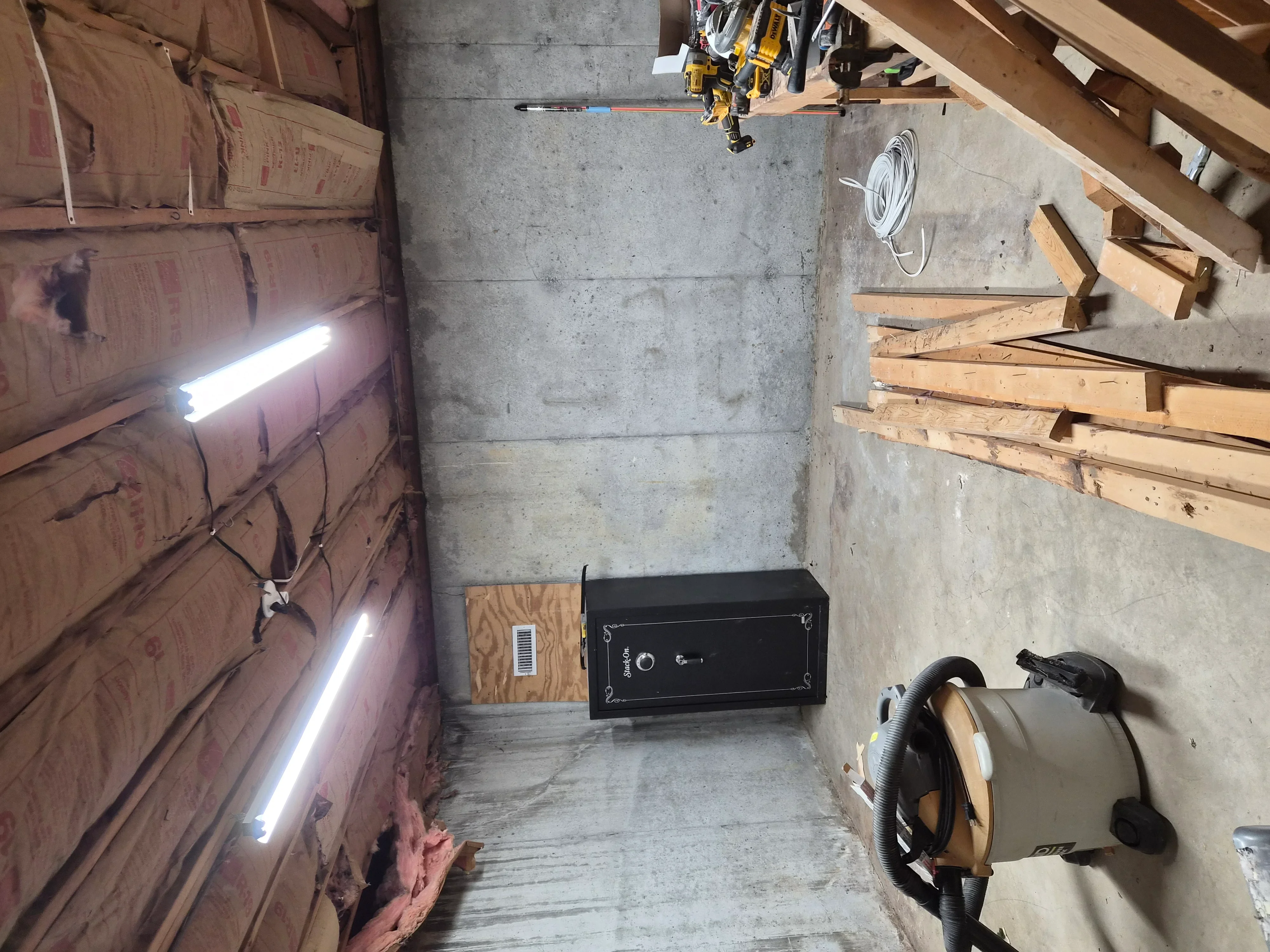 Basement with concrete walls, wood framing, pink insulation batts, and LED lighting installed