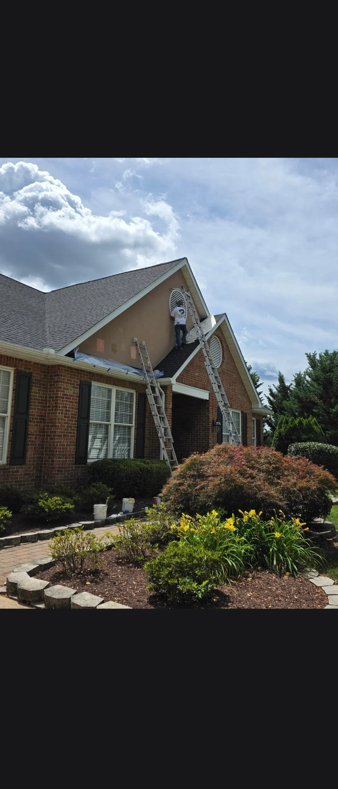 Painter on ladder applying exterior paint to brick home gable section with trim work