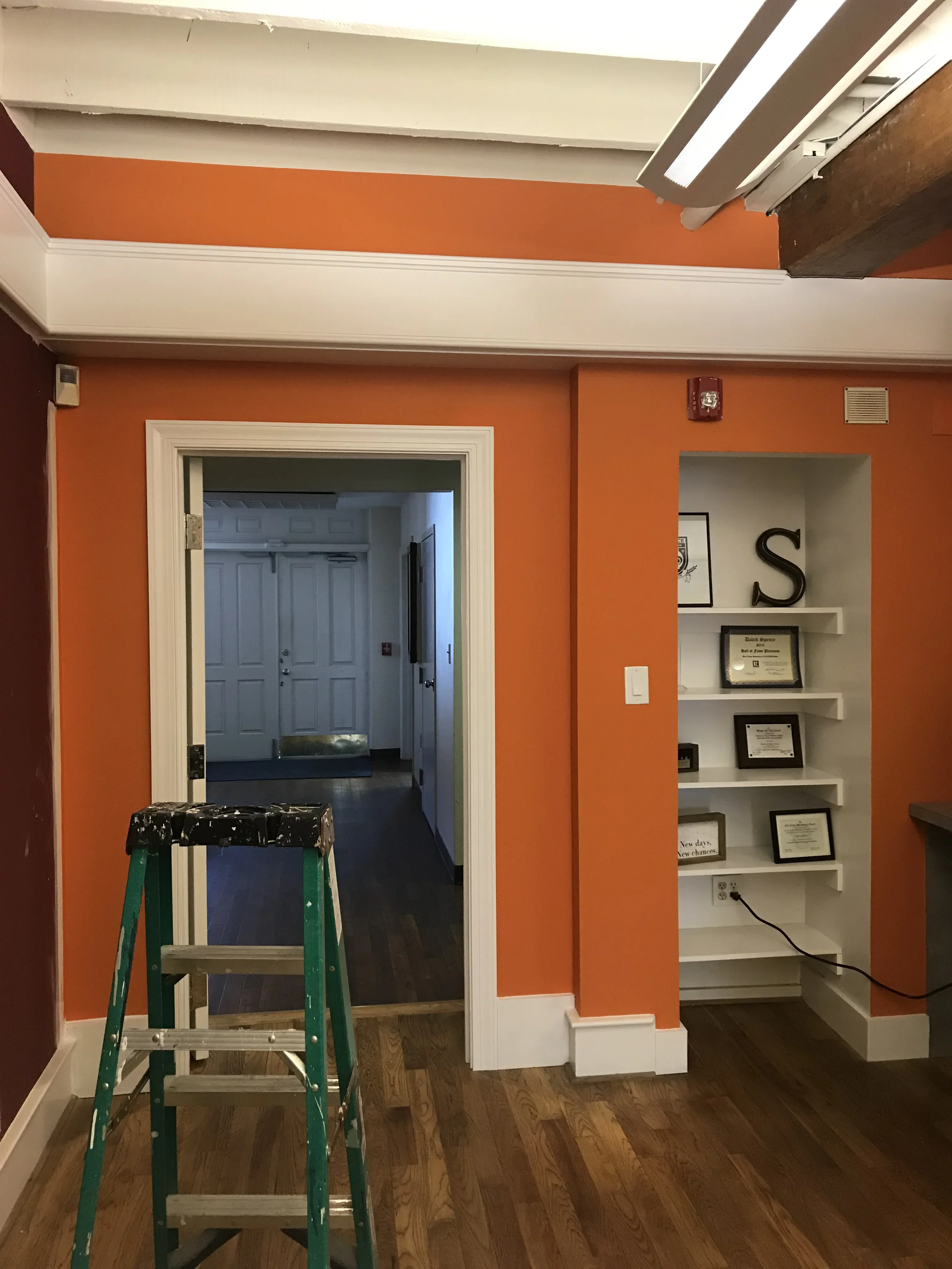 Orange accent wall with white trim, baseboards, and built-in shelving unit in office space