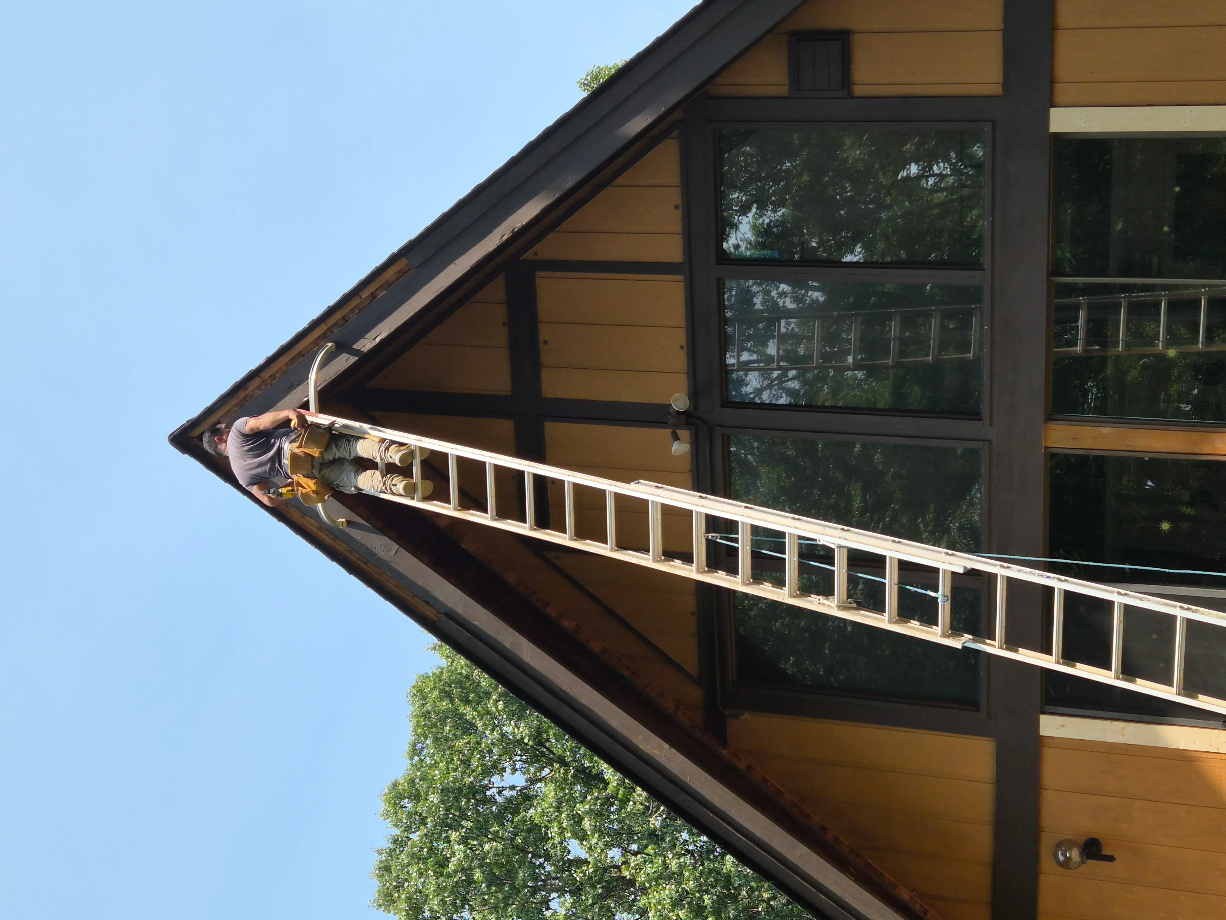 Painter on ladder applying paint to white soffit and fascia trim on residential home exterior
