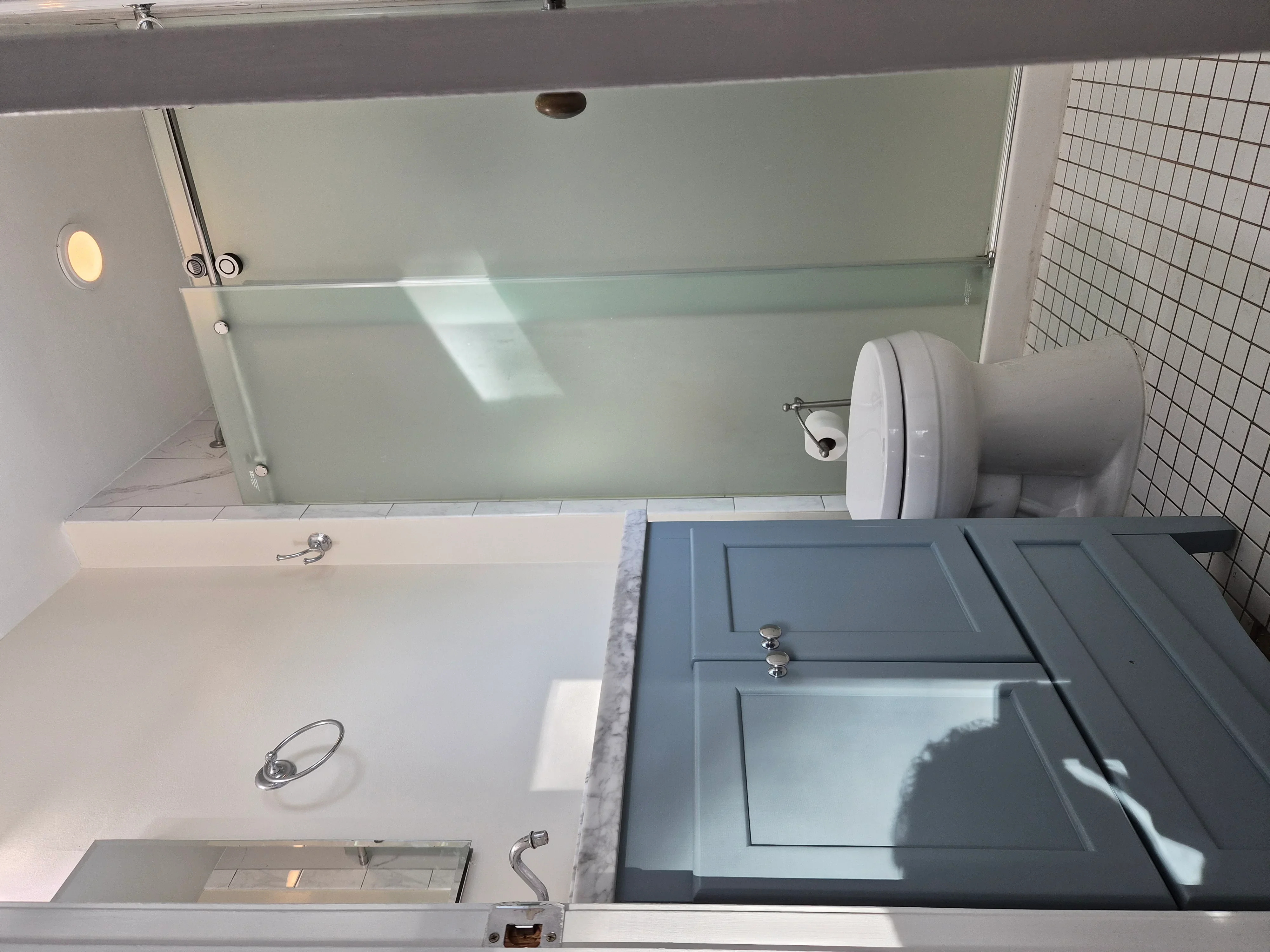 Painted blue bathroom vanity with white trim, frosted glass shower enclosure, and white subway tile walls