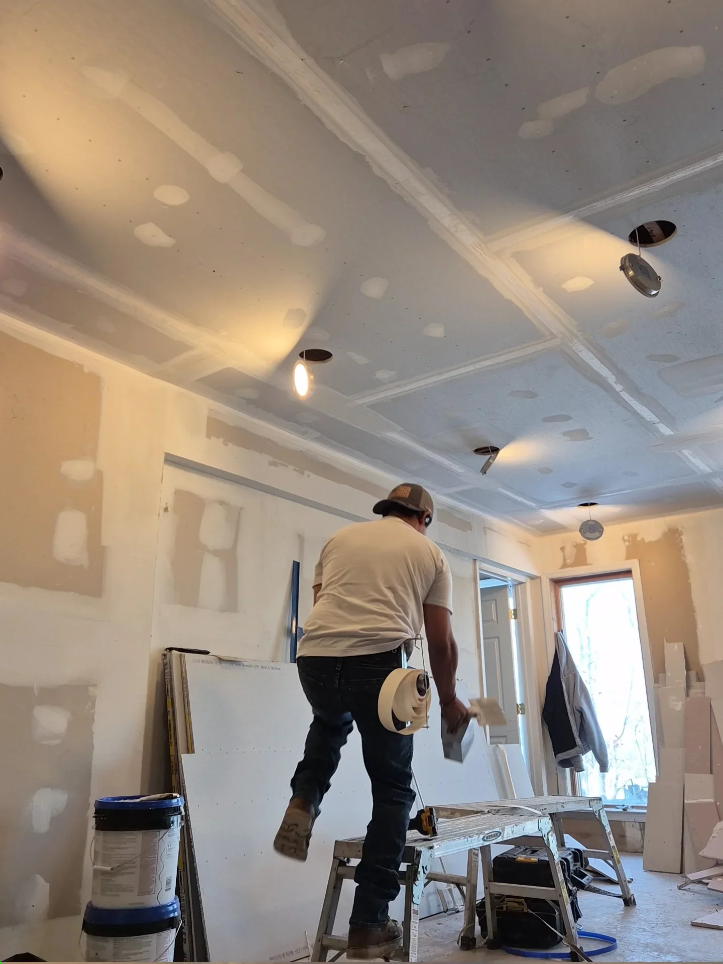 Worker applying joint compound to drywall ceiling and walls with recessed lighting installation