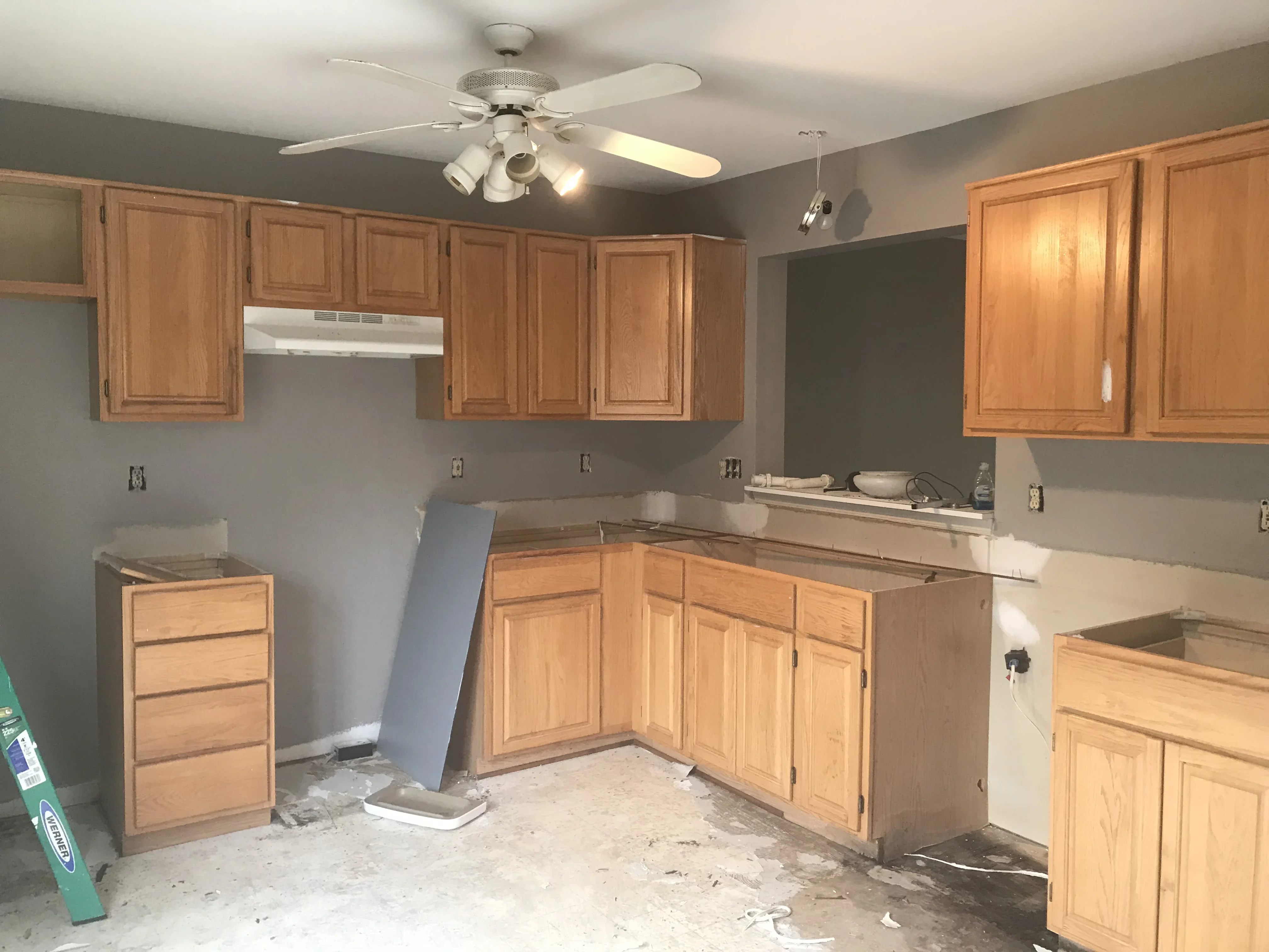 Gray painted kitchen walls with white ceiling, wood cabinets, and ceiling fan during painting project