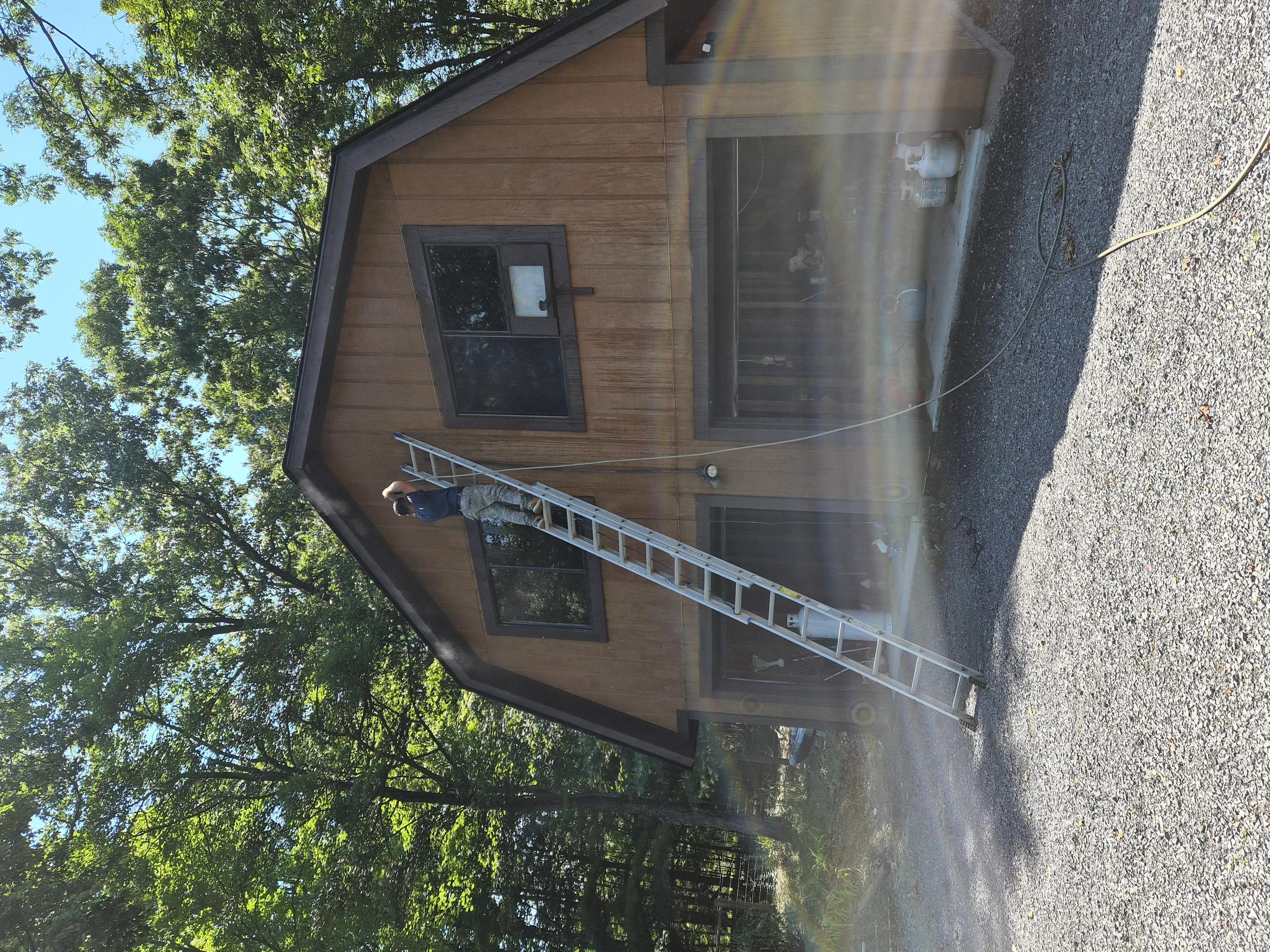 Exterior home with freshly painted cedar wood siding, black-trimmed windows, and aluminum ladder against wall