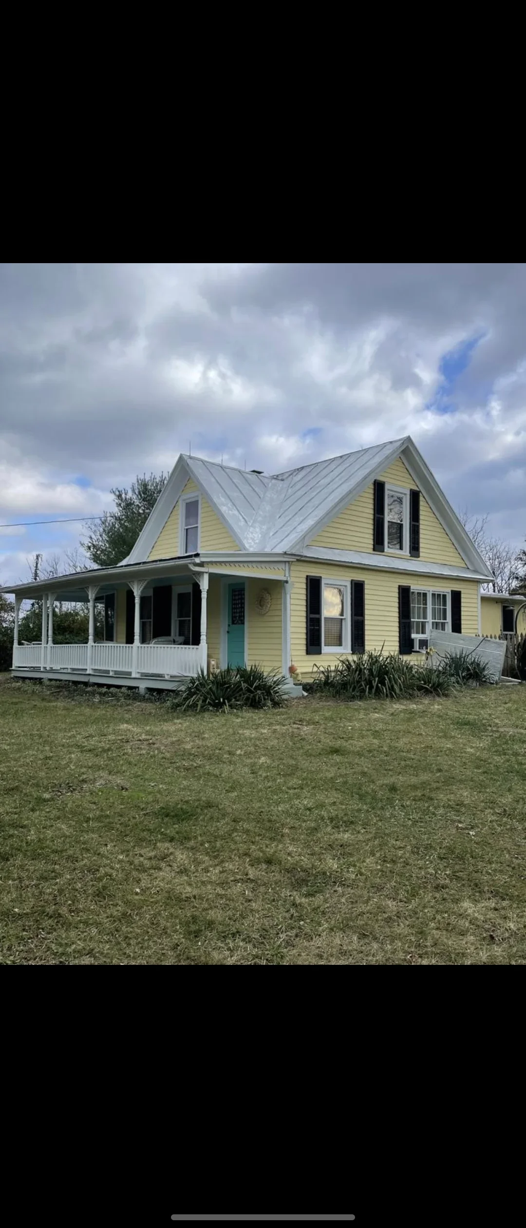 Yellow farmhouse with white porch, metal roof, and black shutters after exterior painting