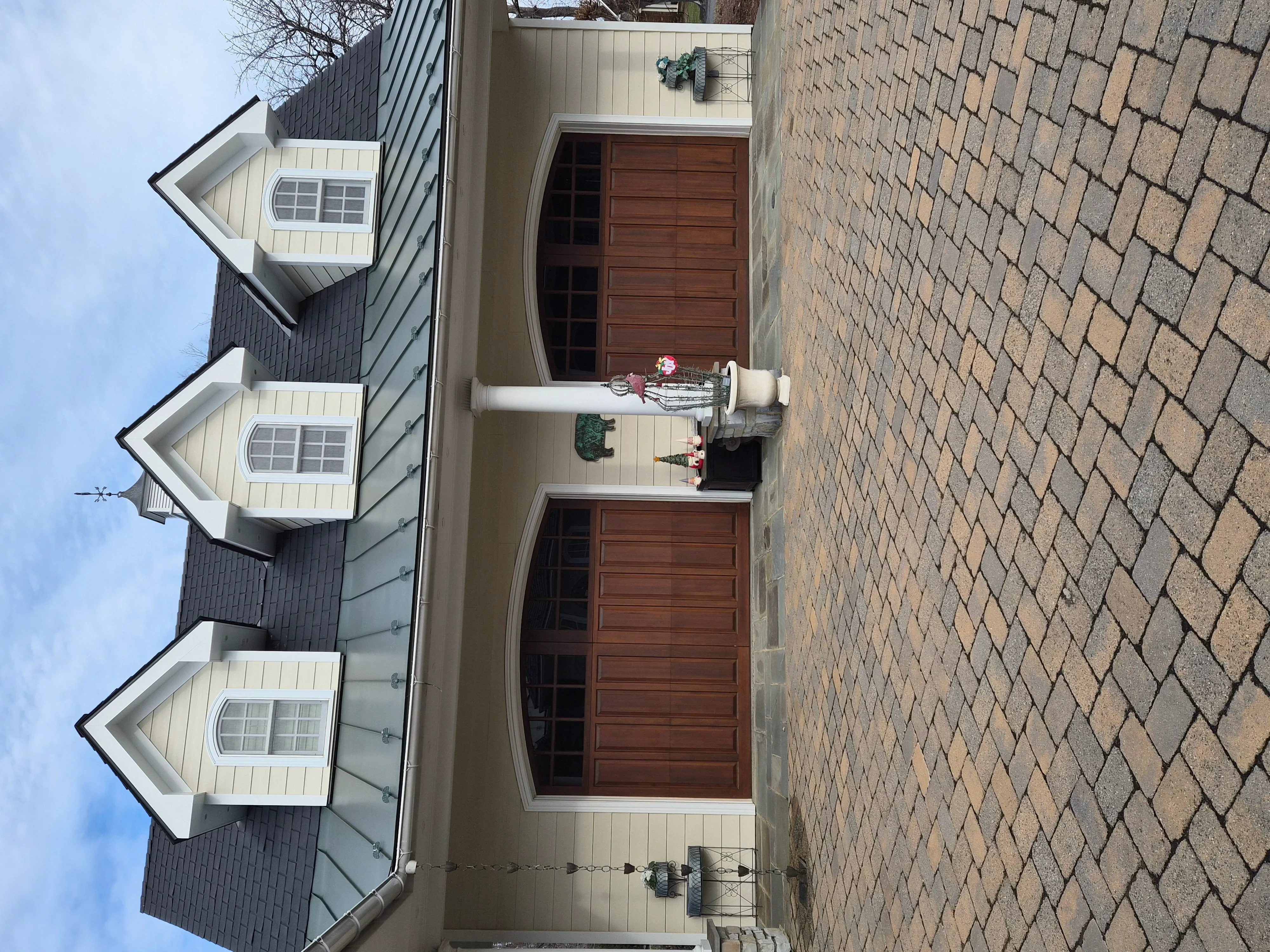 Cream and dark gray vertical siding with white trim, painted dormers, and brown garage doors
