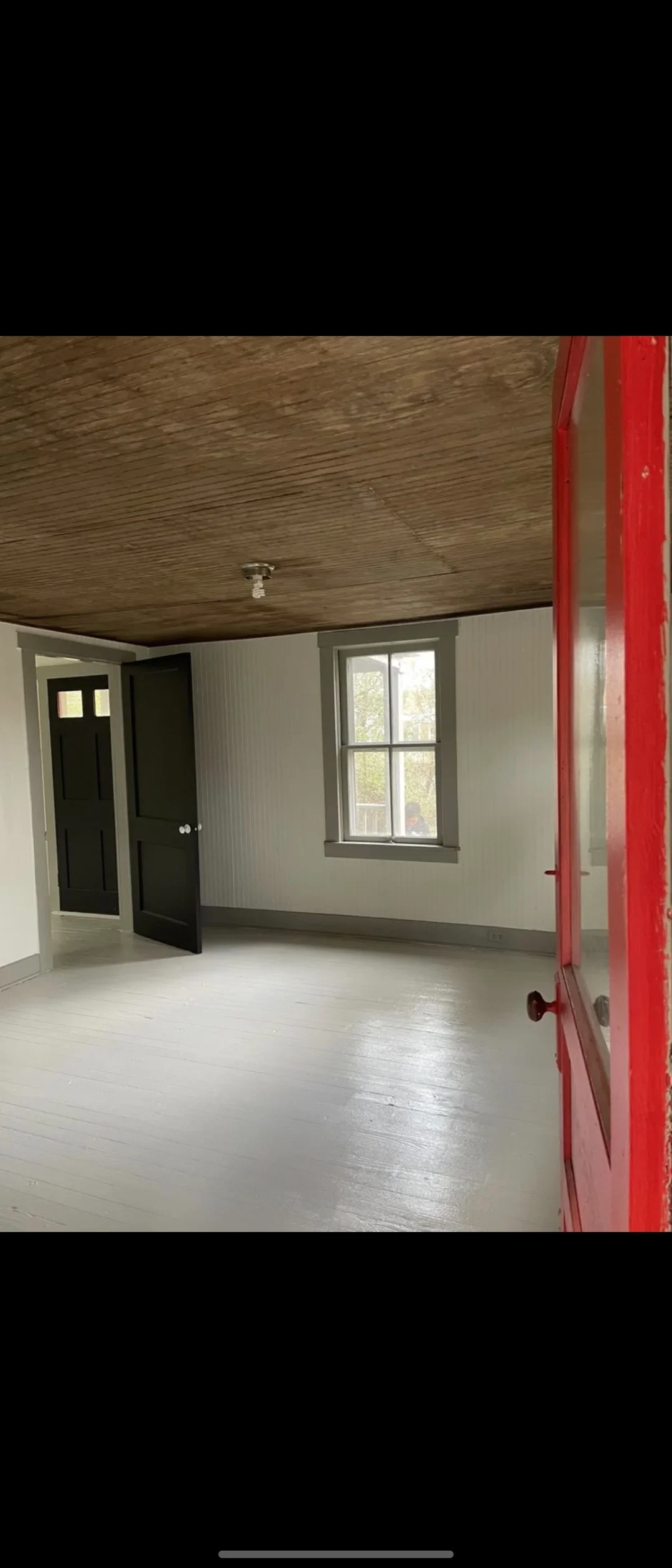 Interior room with white painted drywall walls, wood ceiling, black doors and trim, and window frame