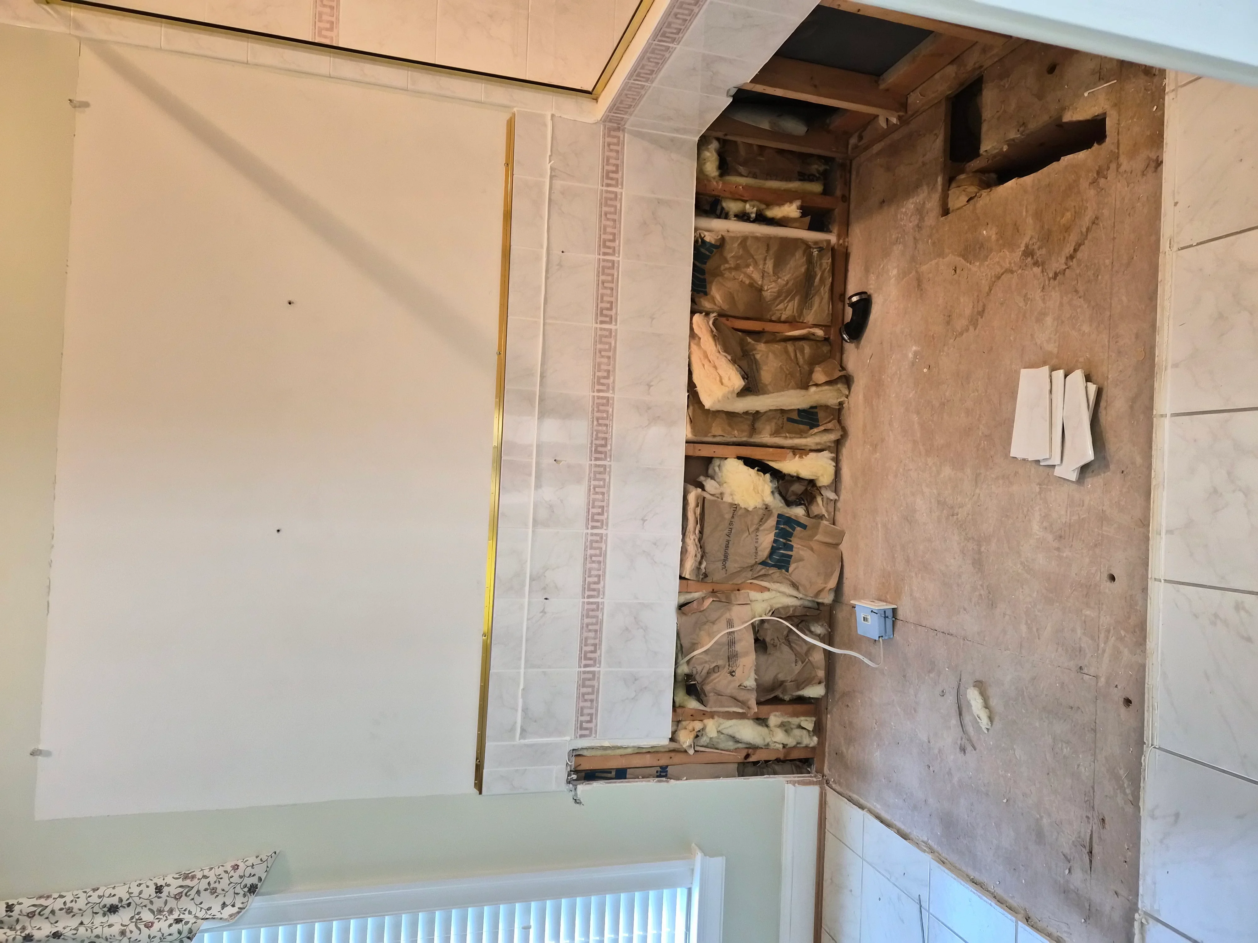 Bathroom under renovation with new drywall, exposed framing, and tile prep work visible