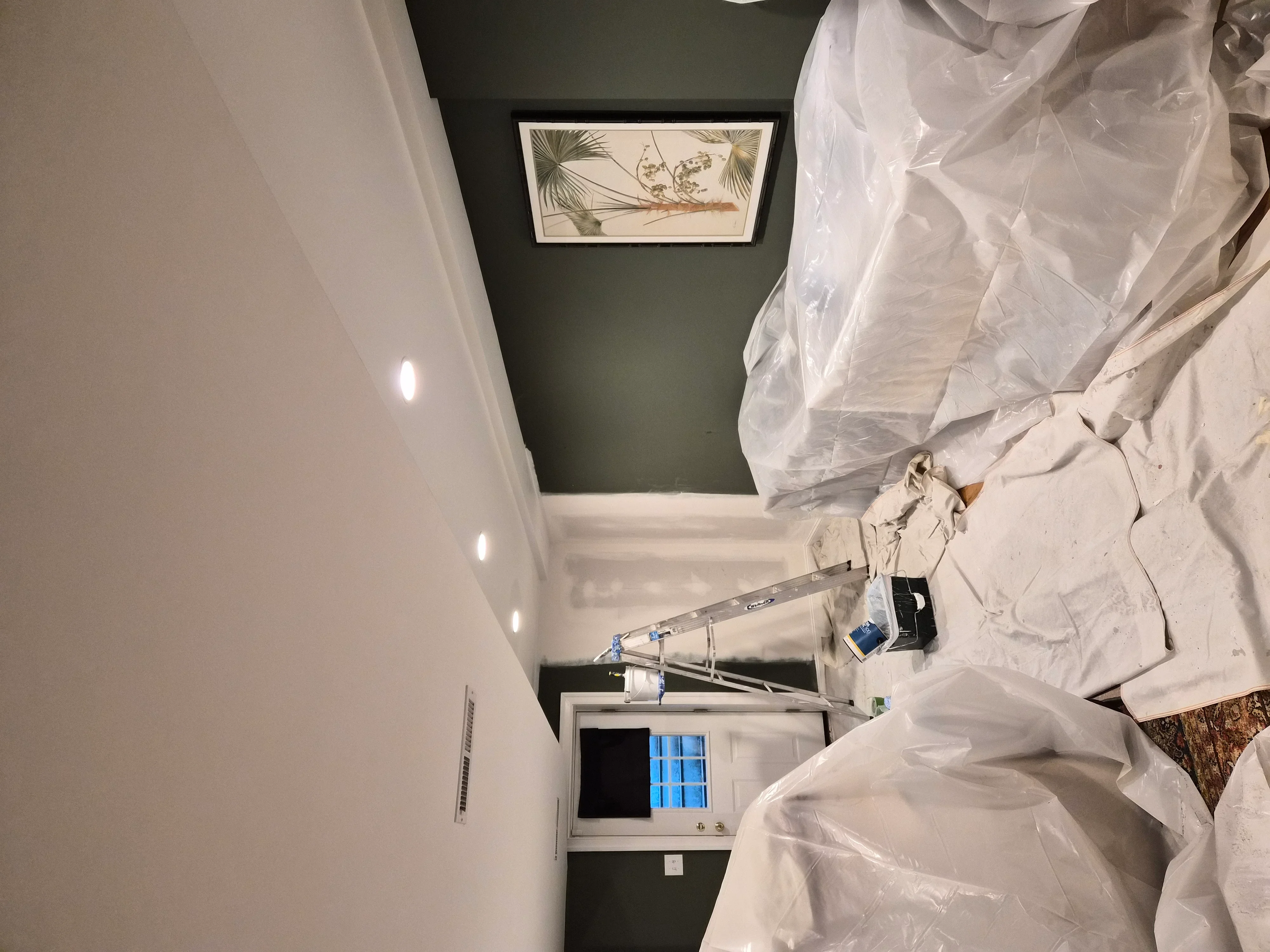 Sage green accent wall with white walls, recessed lighting, and framed art during interior painting project