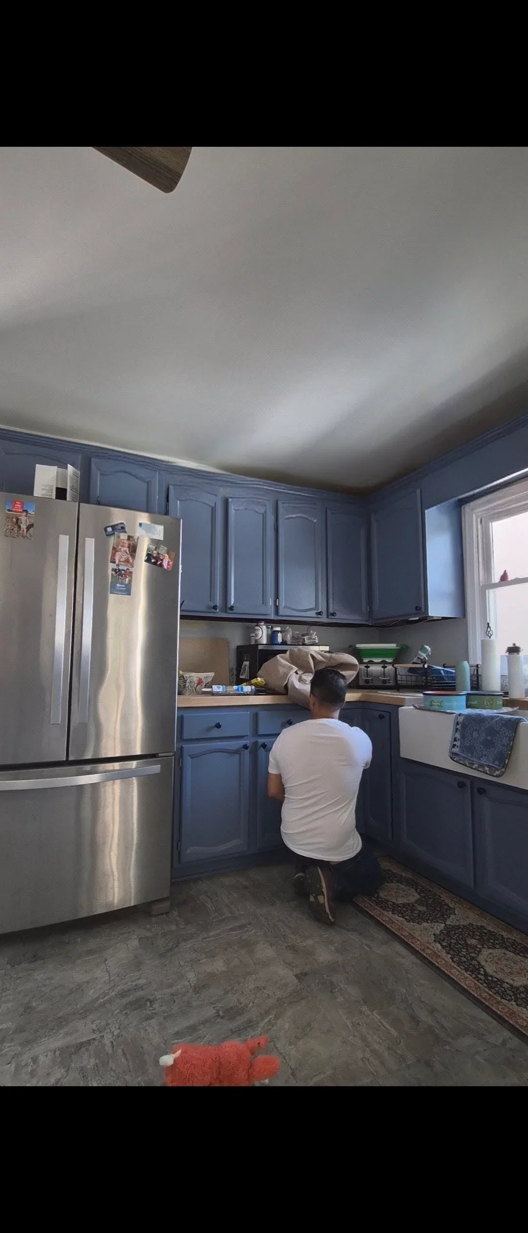 Blue painted kitchen cabinets with stainless steel refrigerator and white ceiling
