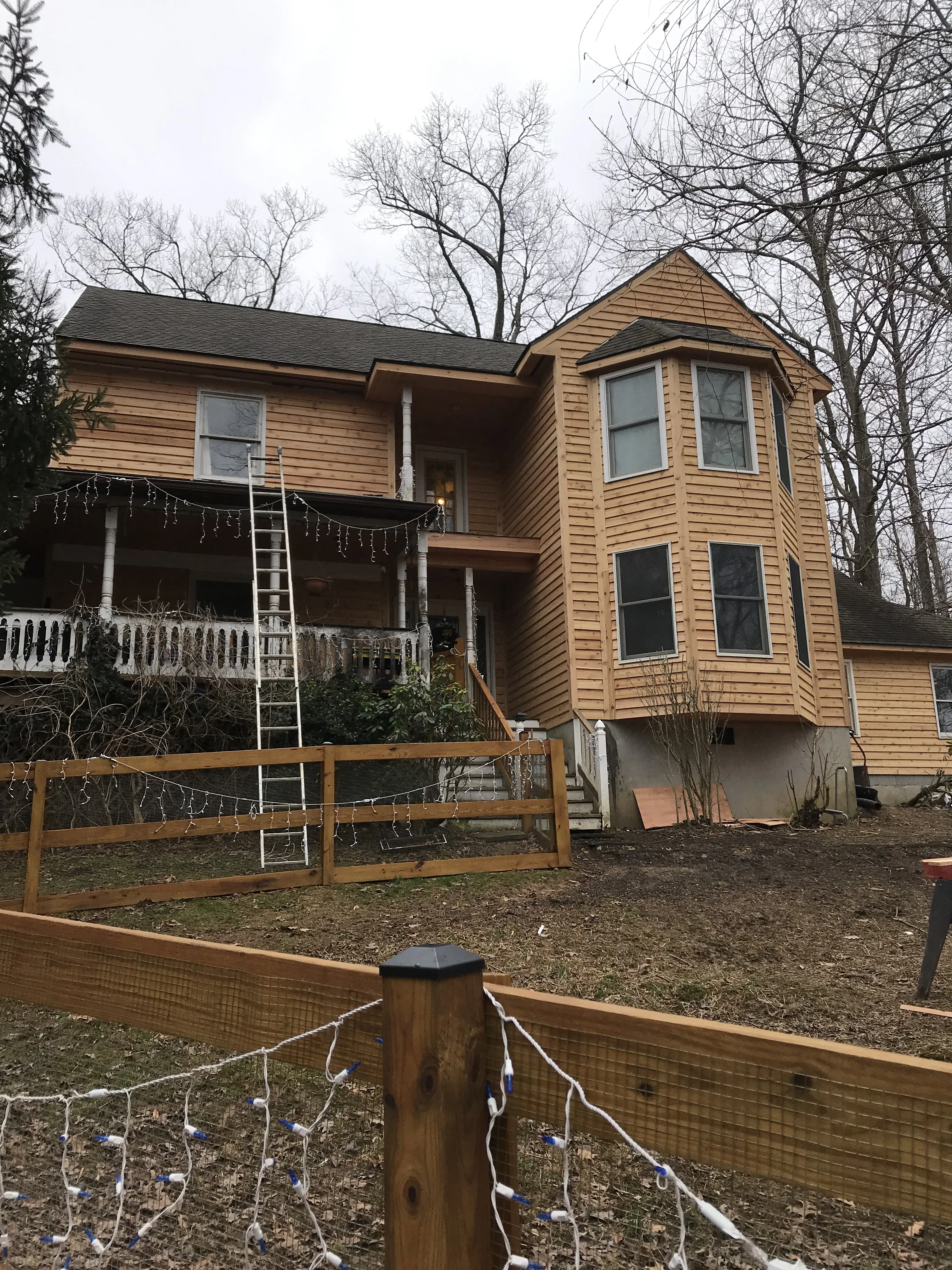 Two-story home with tan lap siding, bay window, and front porch with white railings