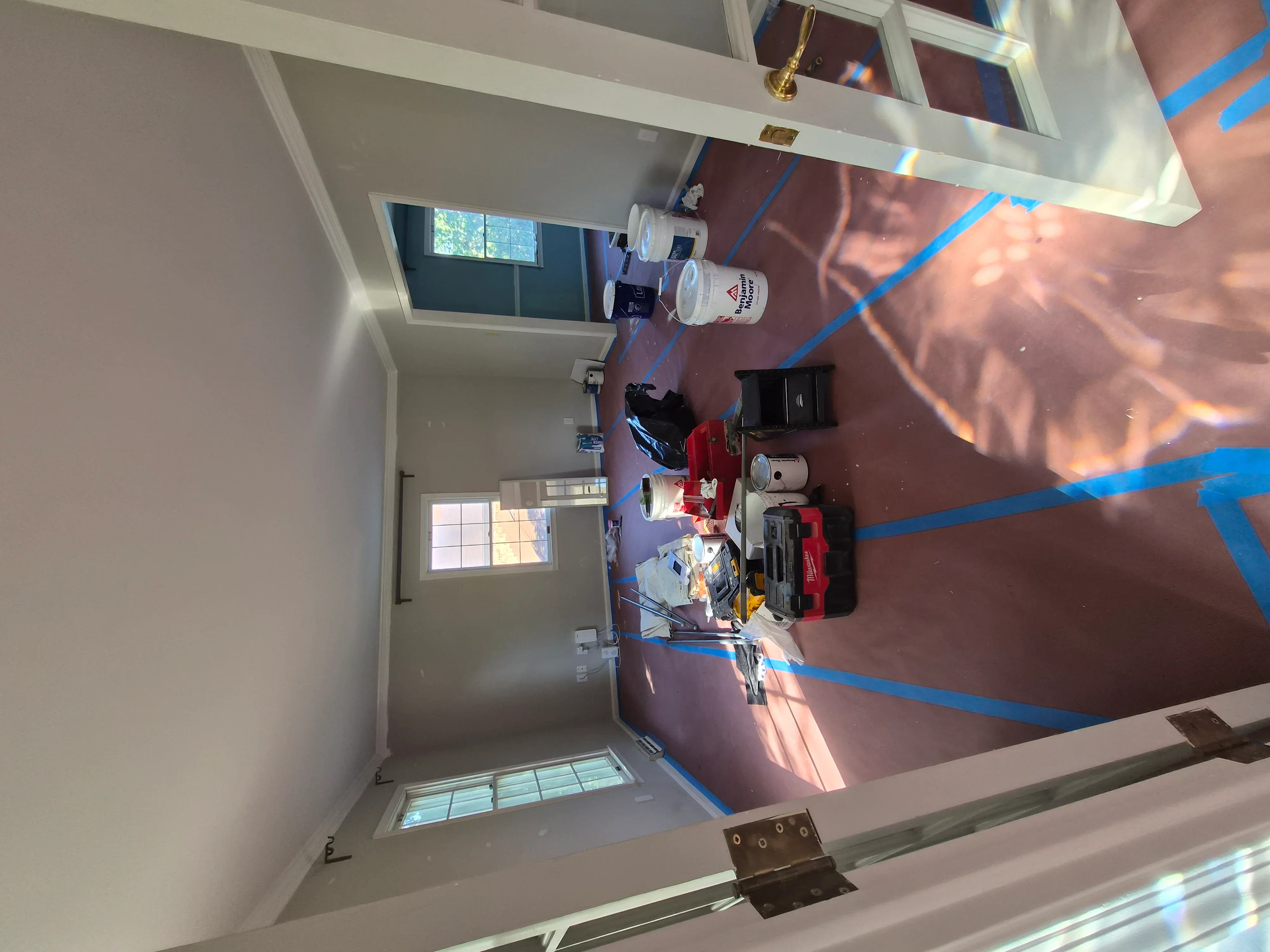 Interior room with freshly painted white and mauve walls, blue painter's tape, and drywall preparation
