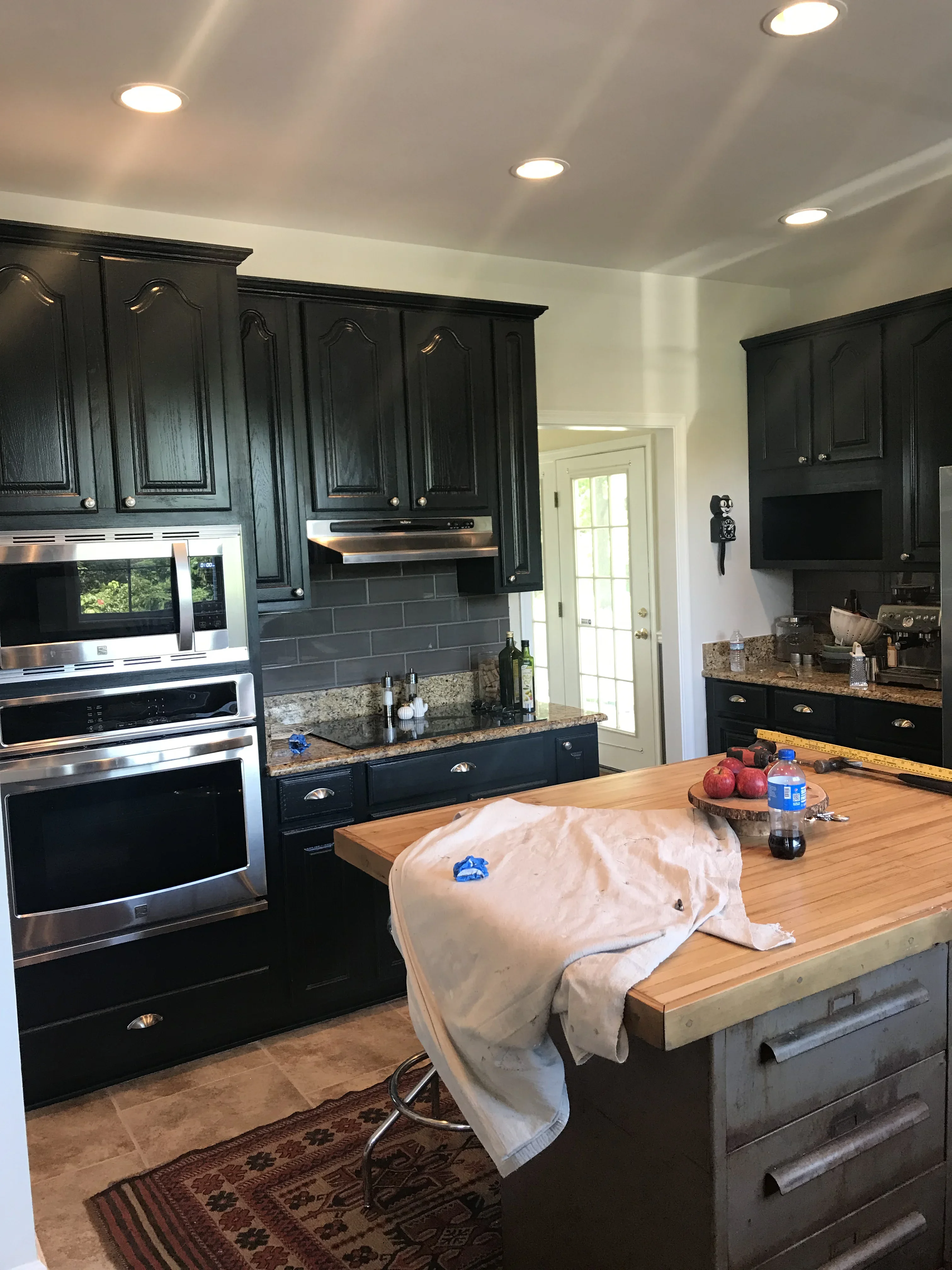 Black painted kitchen cabinets with granite countertops, gray subway tile backsplash, and recessed ceiling lights