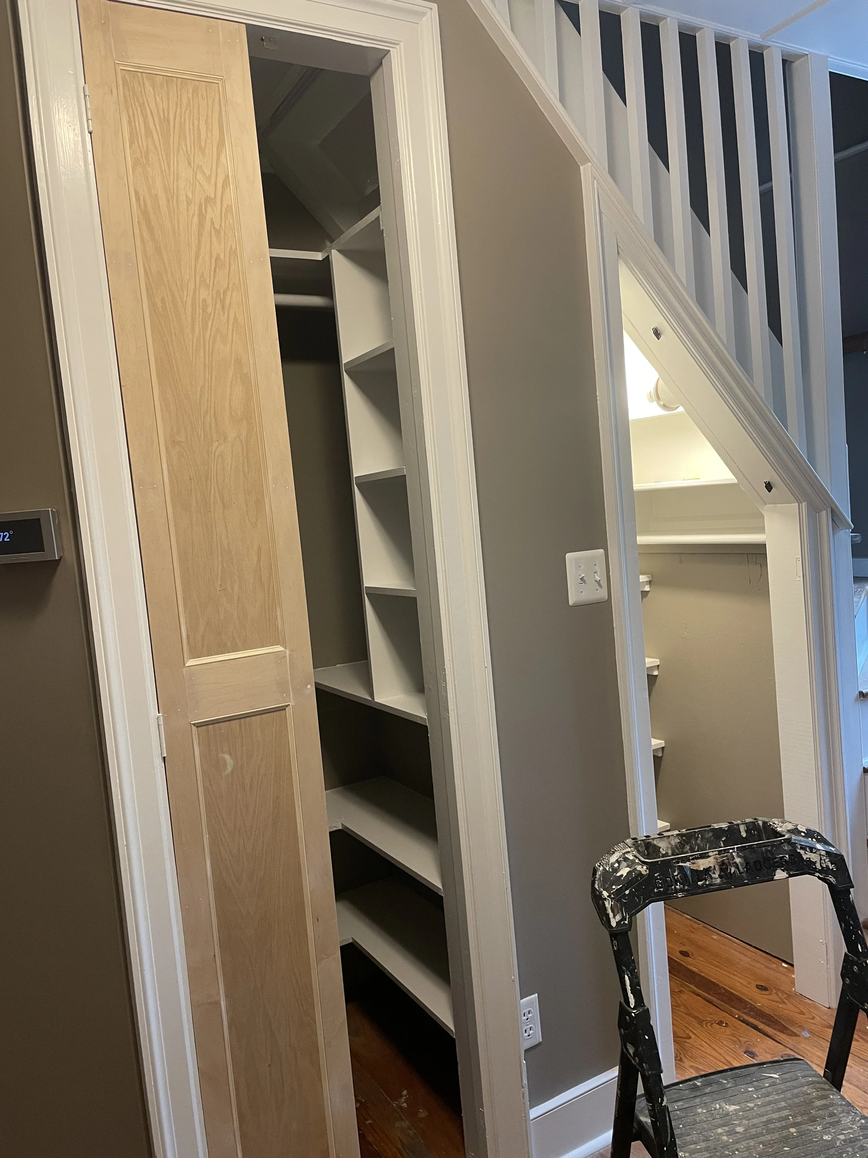 White-trimmed under-stair closet with wood door and built-in shelving