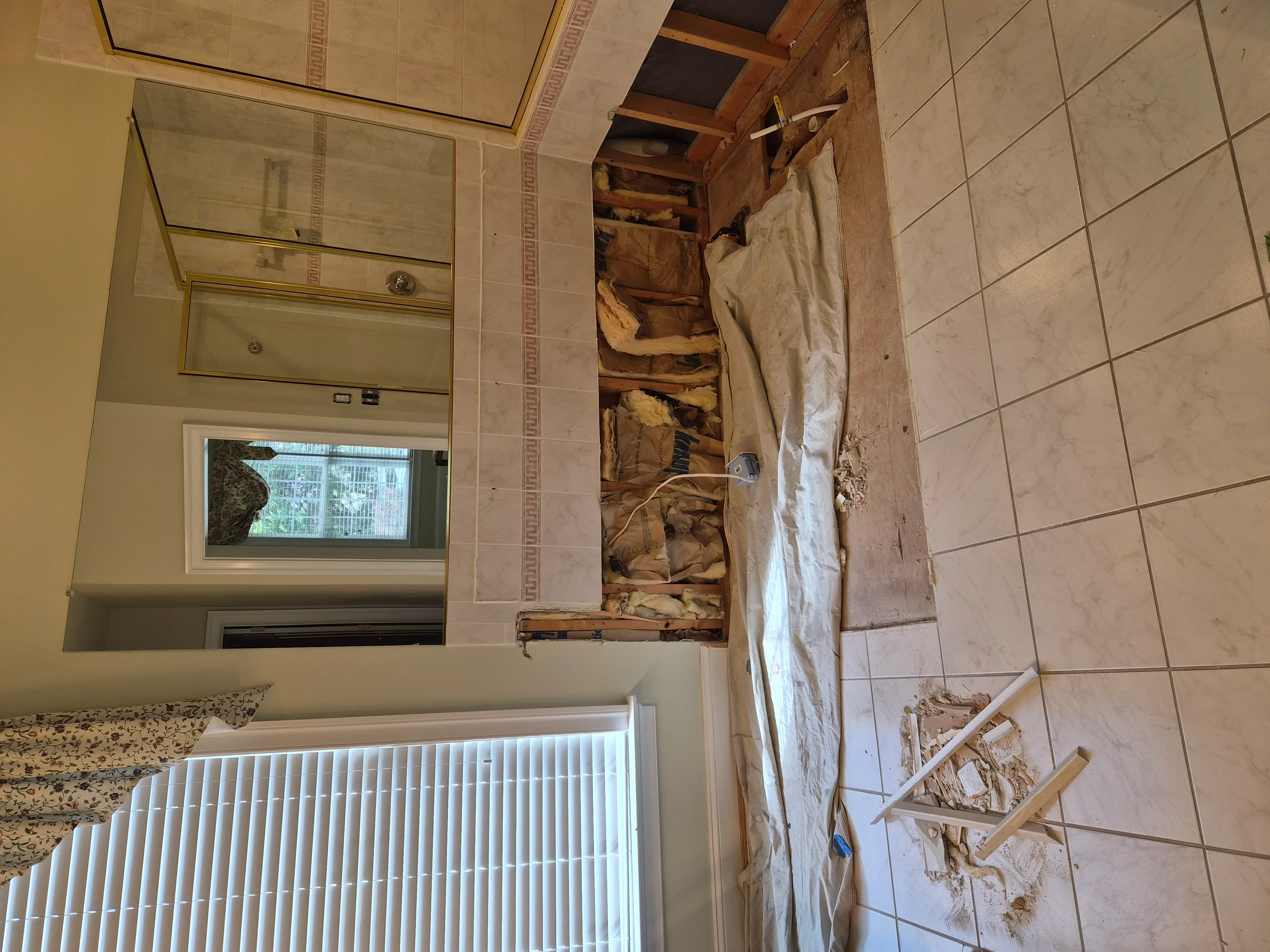 Bathroom with exposed wall framing, ceramic tile, granite counter, and open wall cavity during renovation