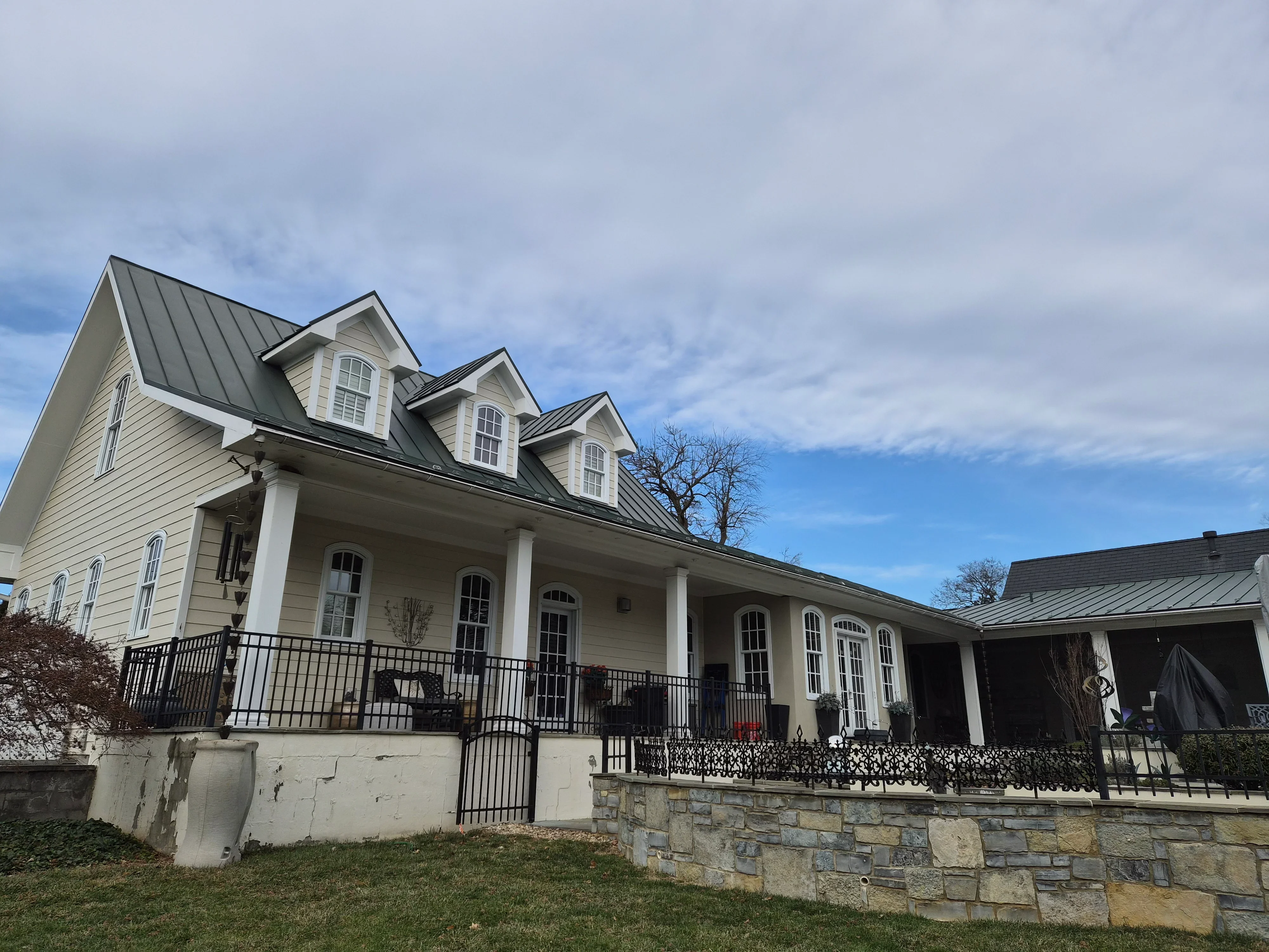 Cream siding and white trim farmhouse with black metal roof and stone foundation wall