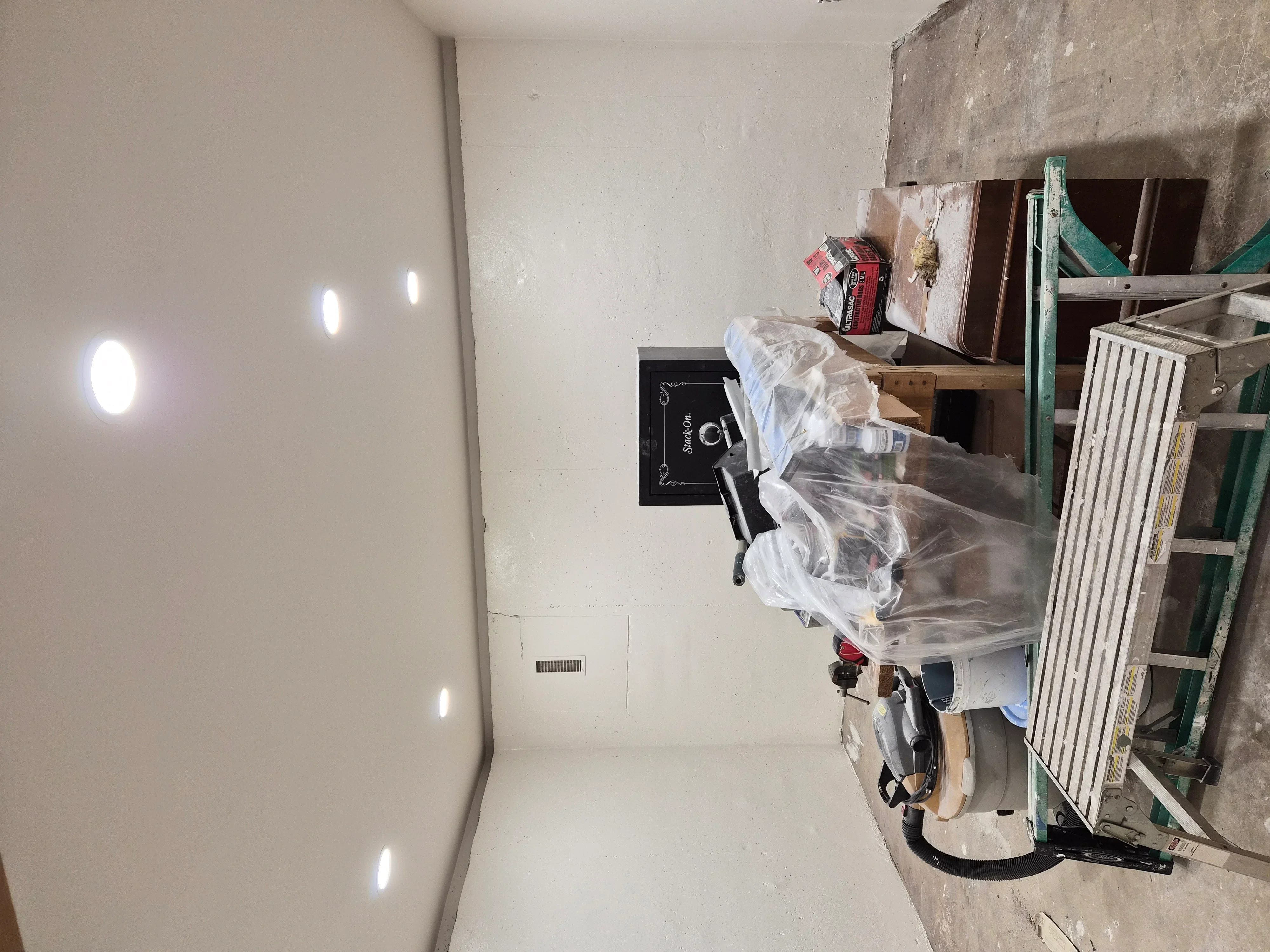Drywall installation with taped seams, mud finishing, and recessed lighting fixtures in interior space